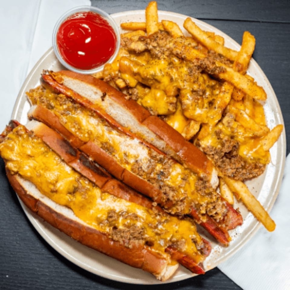 Three chili cheese hot dogs and a side of chili cheese fries with ketchup on a plate.