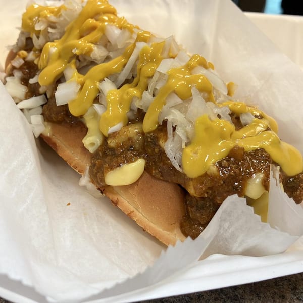 A Jordan's Hot Dogs & Mac chili dog with mustard, chopped onions, and macaroni in a paper tray.